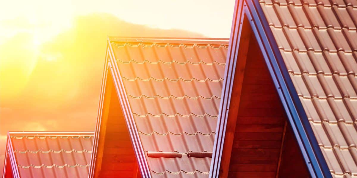 Close-up of multiple pitched metal roofs with sunlight shining in the background.