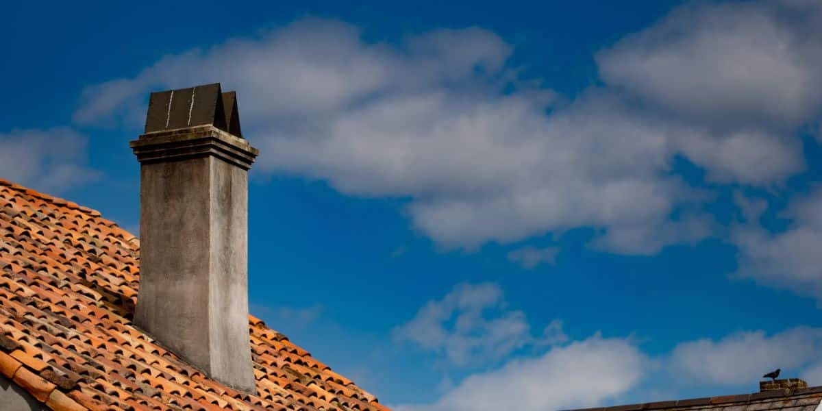 Terracotta tile roof with a chimney against a blue sky with scattered clouds.