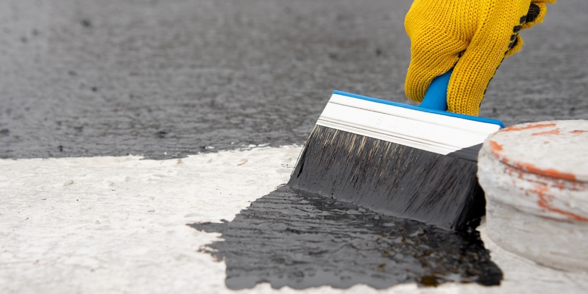 A worker in gloves applying bitumen roof coating with a brush, ensuring a seamless and waterproof protective layer.