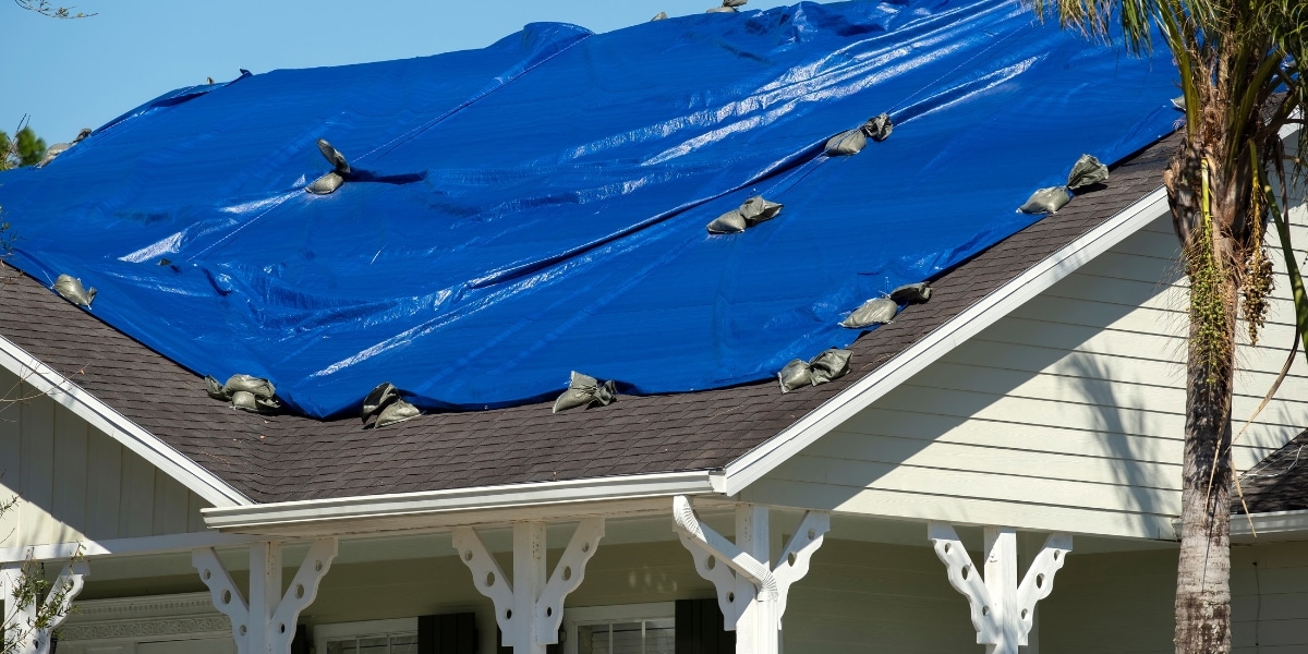 A blue tarp securely covering a roof, fastened with sandbags, after storm damage. Represents Priority Roofing's temporary solutions to stabilize homes during emergencies